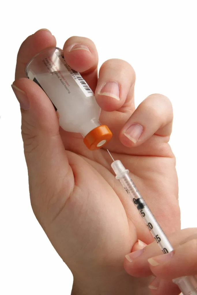 Hand filling syringe with vaccine from vial.