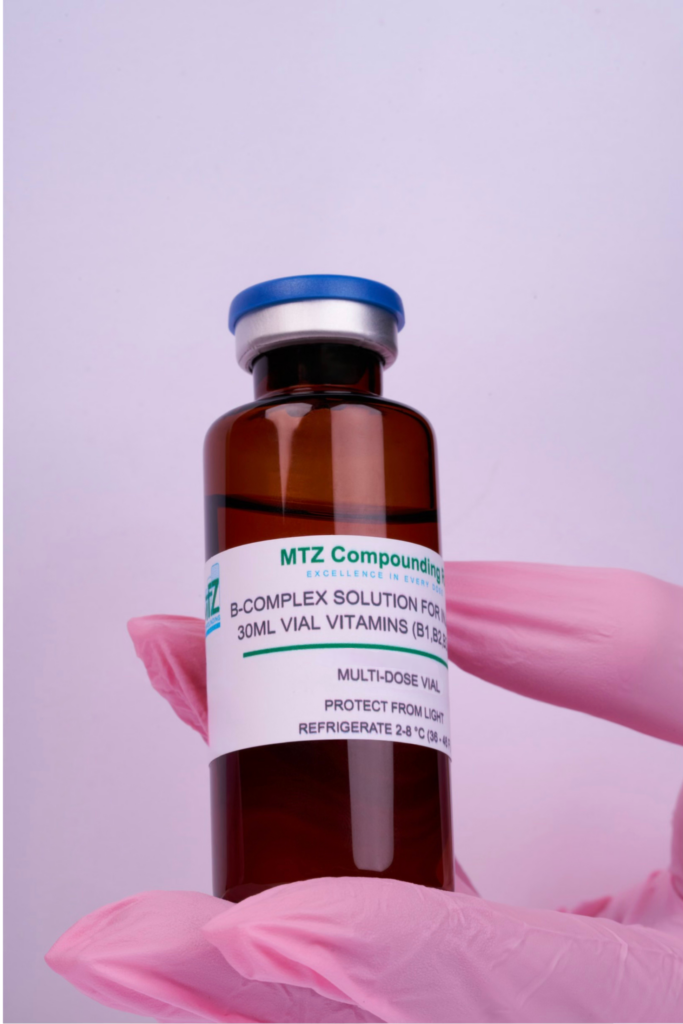 A gloved hand holding a brown medicine vial labeled with vitamins and minerals.
